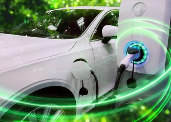 Electric vehicle at charging station with the power cable supply plugged in on blurred nature with green enegy power effect.