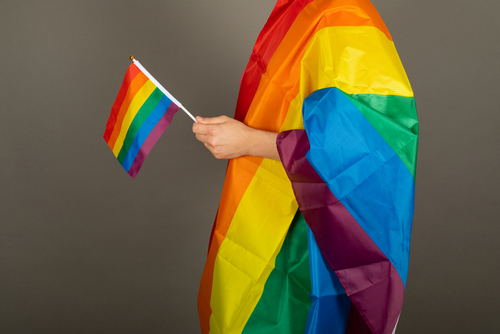 Gay man wearing pink t shirt and a rainbow flag