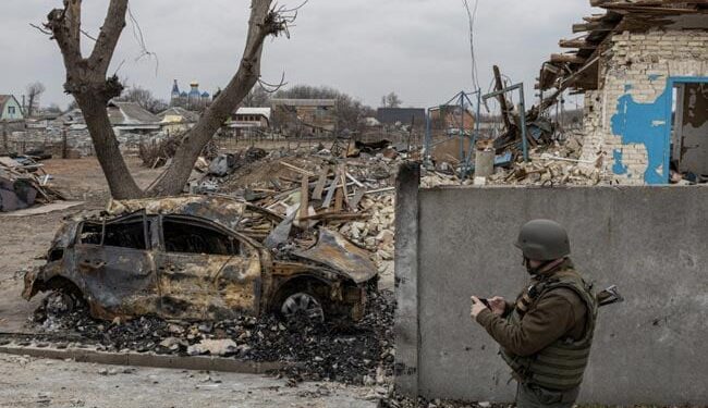 Soldier standing besides a damaged car in Mariupol