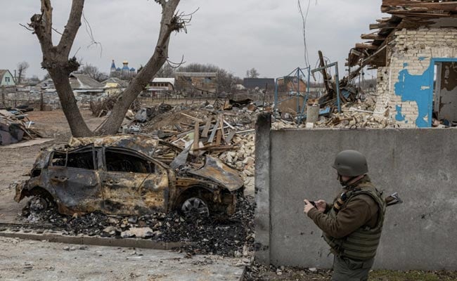 Soldier standing besides a damaged car in Mariupol