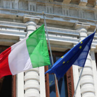 Big,Italian,Flag,And,European,Community,Flag,Flying,Outside,The