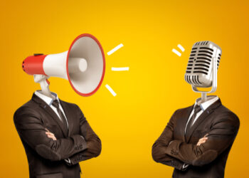 Waist-deep view of two businessmen standing in half-turn, arms folded, with megaphone and microphone instead of heads. Opinion leaders. Media influence public opinion. Media and people.