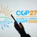 June 15, 2022, Brazil. In this photo illustration, a woman's silhouette holds a smartphone with the 2022 United Nations Climate Change Conference COP27 logo in the background