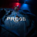 Freedom of the press and journalism concept. Blue journalist (press) vest in dark with backlight and fog. Microphone and handcuffs. Selective focus