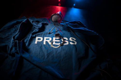 Freedom of the press and journalism concept. Blue journalist (press) vest in dark with backlight and fog. Microphone and handcuffs. Selective focus
