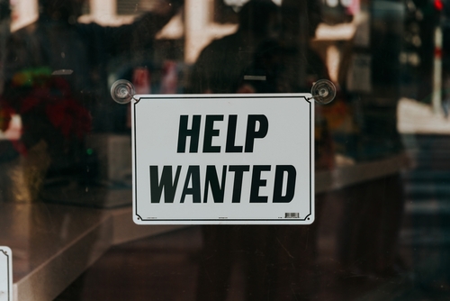 A sign on a store front glass window saying "Help Wanted"