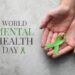 World Mental Health Day. Woman holding green ribbon at grey table, top view