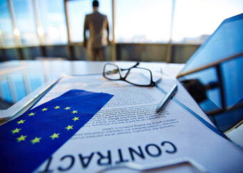 International contract with pen, flag of European Union, digital tablets and eyeglasses with office worker on background