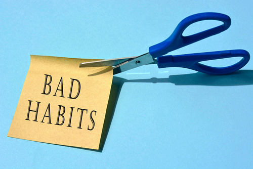 Scissors that cut yellow notepad with bad habits text on a blue background. Spending concept