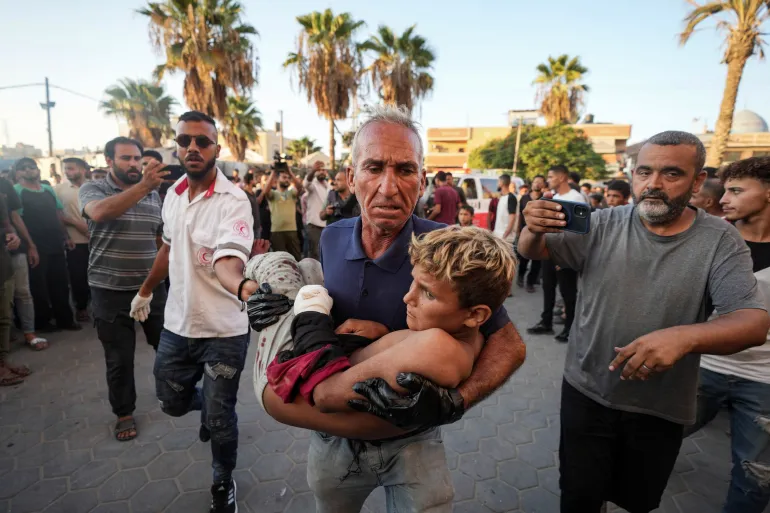 Palestinian man carries an injured child after an Israeli airstrike
