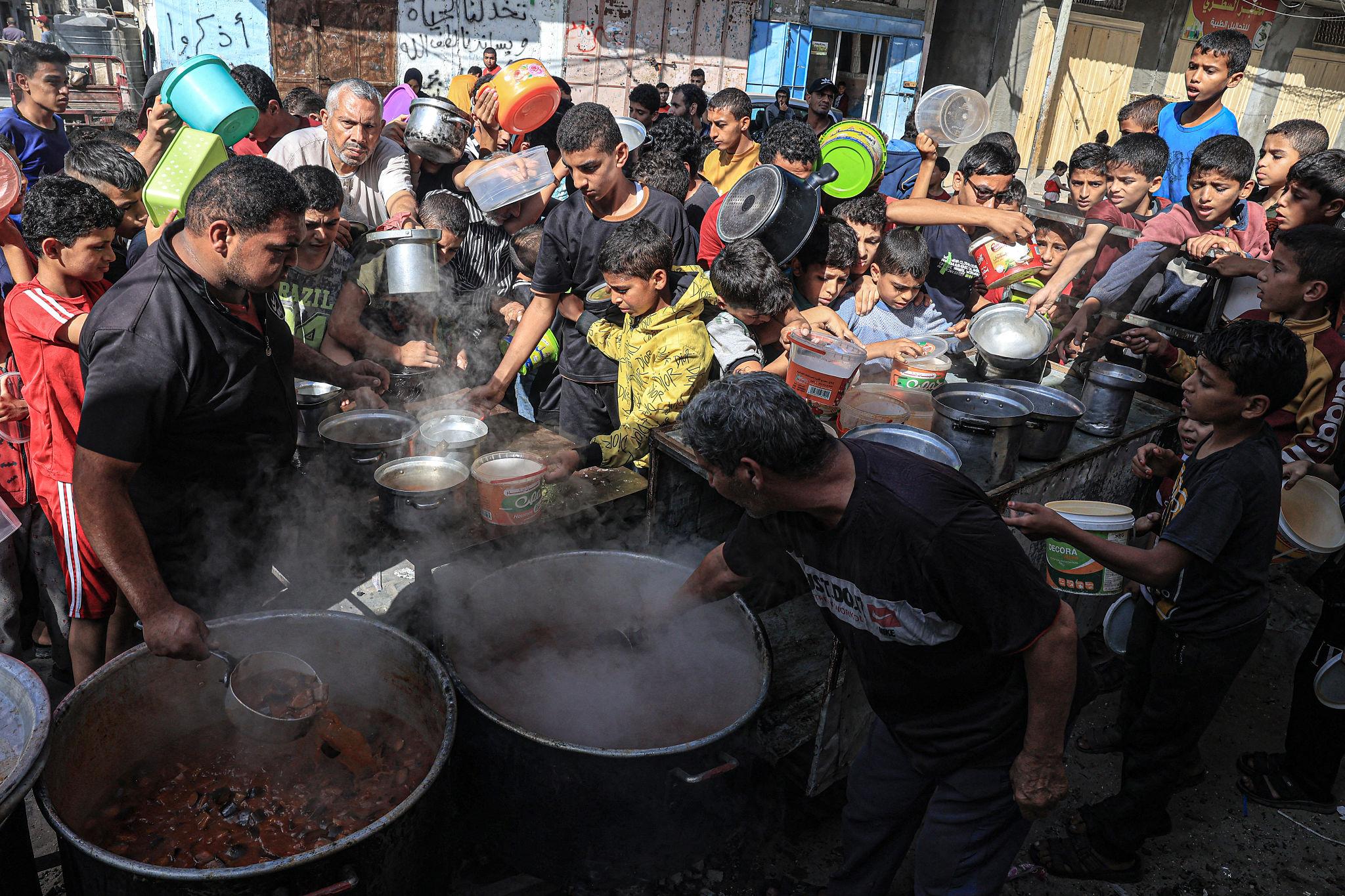 Displaced Palestinians waiting for warm meals at food distribution point in Gaza
